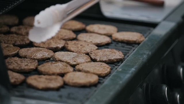 Close up of burgers frying on a grill. Chef cooking tossing and flipping by spatula juicy meat cutlet.