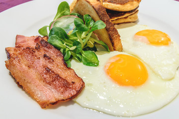 American breakfast  with sunny side up eggs, bacon and french toast, close up photo