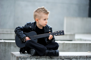 A handsome boy in black leather jacket, with  iroquois haircut, playing rock music on the guitar,...