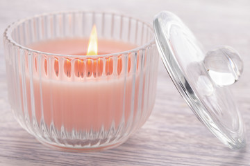 Pink candle burning in a glass beaker on an old white wooden table.