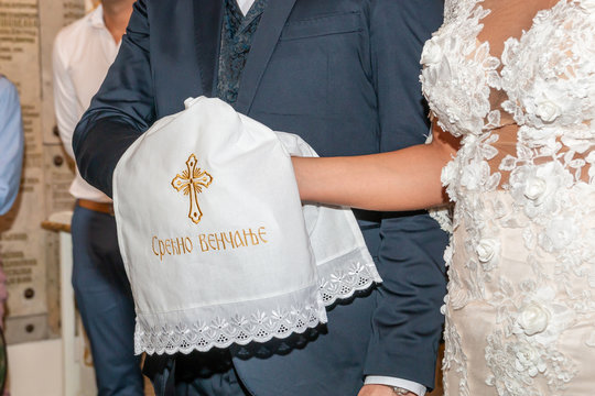 Traditional wedding handfasting in orthodox church. Hands of the bride and groom are tied with a wedding embroidered towel. Inscription "Срећно венчање"  means "Happy wedding".