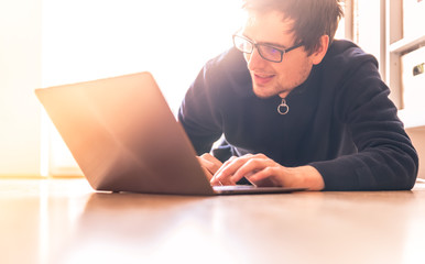 Happy young man with a modern laptop is sitting on the wooden floor