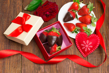 Box with tasty chocolate dipped strawberries and bouquet of flowers on table