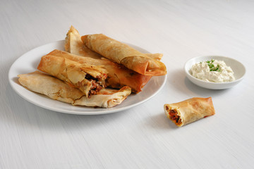 filo or yufka dough rolls stuffed with a spicy meat filling and cheese curd on a white painted table, copy space