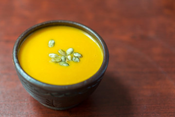 Pumpkin cream-soup with addition of pumpkin seeds and spices, view from above, studio shot. Clay plate of pumpkin cream-soup with addition of pumpkin seeds and spices, above view. copy space.