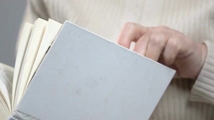 Elderly female retiree in glasses reading book at leisure time, hobby and relax