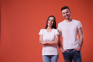 Beautiful young couple in white blank t-shirts are posing on orange background. Relationship, family, advertising