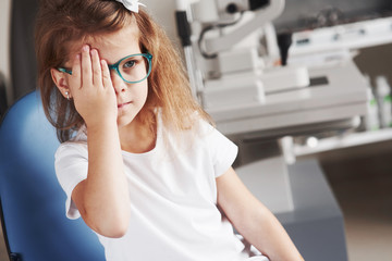 Close right eye with your hand. Little girl checking his vision with new green glasses