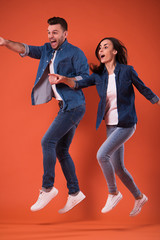 Full length portrait of a cheerful and excited young couple jumping together and celebrating success while running isolated in studio