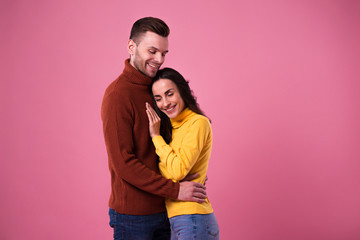 Young cheerful loving couple dressed in sweaters hugging isolated over pink background