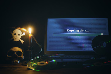 Illegal data copying concept. Cybercrime. Computer piracy background. Pirate hat, human skull, laptop and compact disc on a table.