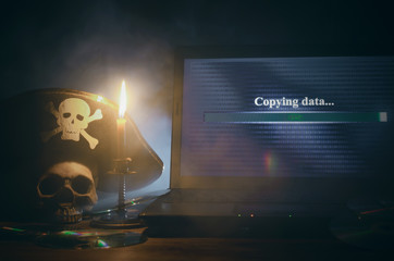 Fototapeta premium Koncepcja nielegalnego kopiowania danych. Cyberprzestępczość. Piractwo komputerowe tło. Piracki kapelusz, ludzka czaszka, laptop i płyta kompaktowa na stole.