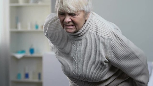Young medical worker helping senior female suffering ache in back to stand up
