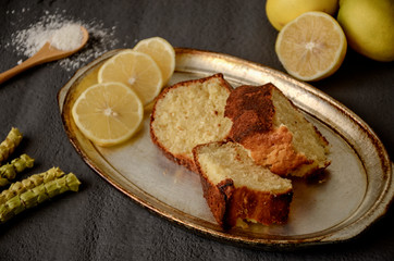 Classic lemon pound cake on rustic grey background with slices of lemon
