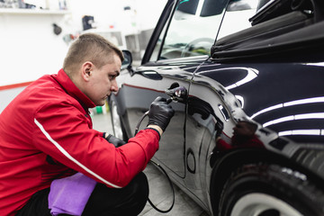 Fototapeta na wymiar Car detailing - Worker with orbital polisher in auto repair shop.