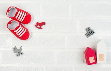 Baby booties and wooden toys on white brick background