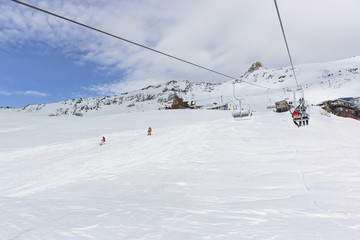 Fototapeta na wymiar A two-seat cable car and a ski track with snowboarders in the ski resort of Dombay in the middle of the winter season