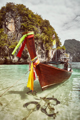 Retro toned picture of a long tail boat moored by a tropical island, Thailand.