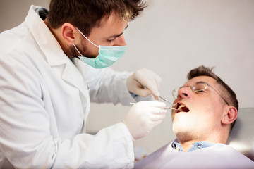 Obraz na płótnie Canvas Serious young male dentist examining mature male patient in dental clinic