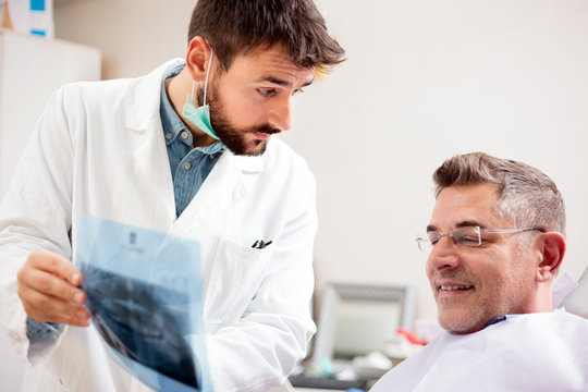 Serious young male dentist showing x-ray images to a mature male patient. Dental exam in medical clinic