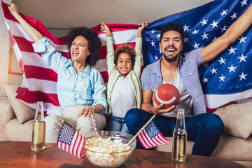 Happy African American family of three watching tv and cheering sport games on sofa at home