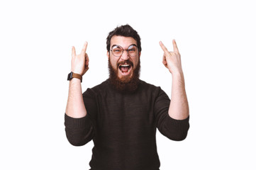 Fototapeta premium Excited bearded guy with crazy face expression is going rock symbol with hands up