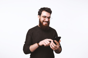 A smiling bearded man wearing glasses is scrolling texting in his cellphone