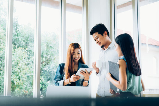 Young asian casual business team happy smiling while standing relax meeting about marketing on digital tablet in modern coworking space office