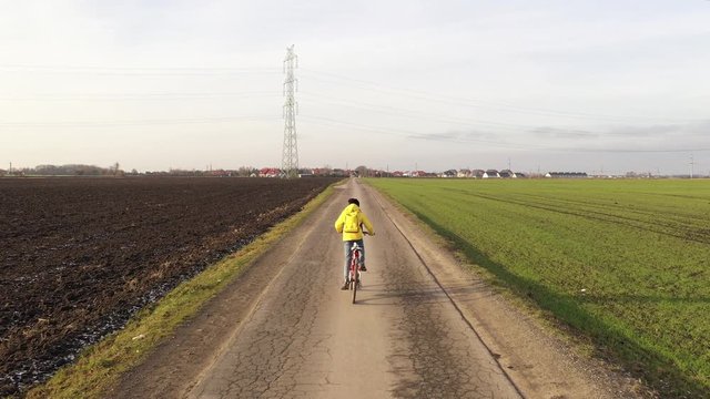 Aerial drone view girl rides bicycle on countryside road in yellow jacket