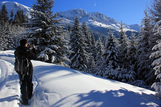 Trekking in the snow. Mountains and forest during winter season. Sunny day in the mountains during winter time. Man making photos. 
