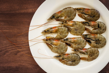 Fresh uncooked king prawns in a white plate on a brown wooden background. Delicacy, tasty and healthy sea food, close up, top view
