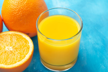 Orange fresh drink, glass of juice and ripe citrus fruits on a blue background