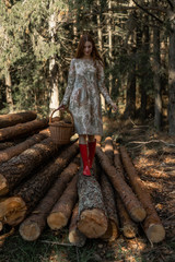 Young woman with long red hair in a linen dress gathering mushrooms in the forest in the bast basket