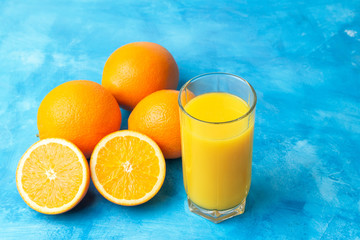 Orange fresh drink, glass of juice and ripe citrus fruits on a blue background