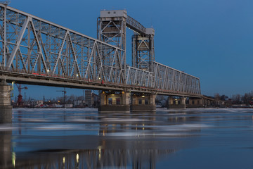 Fototapeta premium Beautiful view of ice drift under the railway bridge in Arkhangelsk, Russia. Beautiful ice motion on Northern Dvina river, evening landscape.