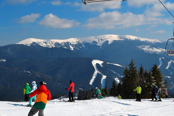 Landscape of winter hills in sunny day. Sport concept. People in colorful sportwear are skiing down...