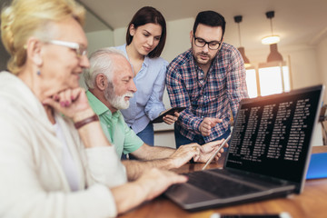 Obraz premium Young volunteers help senior people on the computer. Young people giving senior people introduction to internet