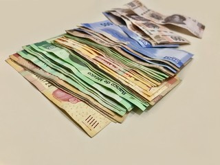 Many mixed Mexican peso bills spread over a beige desk