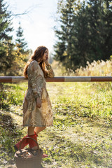 Young woman with long red hair in a linen dress gathering mushrooms in the forest in the bast basket
