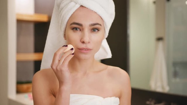 Woman applying foundation on her face using makeup sponge