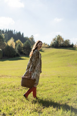 Young woman with long red hair in a linen dress gathering mushrooms in the forest in the bast basket