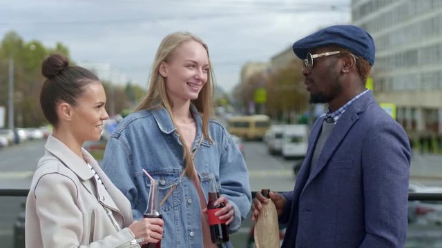 Tilt-up shot of young people standing on the street talking and holding bottles with drinks