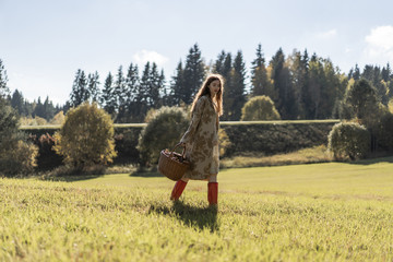 Young woman with long red hair in a linen dress gathering mushrooms in the forest in the bast basket