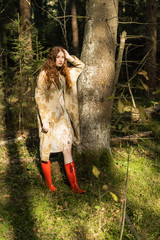 Young woman with long red hair in a linen dress gathering mushrooms in the forest in the bast basket
