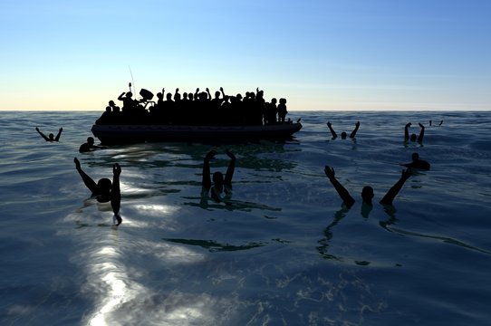 Profughi su un grande gommone in mezzo al mare che richiedono aiuto. Mare con persone in acqua che chiedono aiuto. Migranti che attraversano il mare