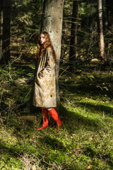 Young woman with long red hair in a linen dress gathering mushrooms in the forest in the bast basket