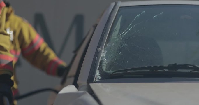 Broken car windshield with firefighters nearby