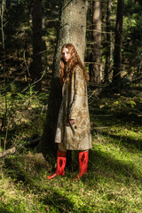 Young woman with long red hair in a linen dress gathering mushrooms in the forest in the bast basket