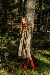 Young woman with long red hair in a linen dress gathering mushrooms in the forest in the bast basket