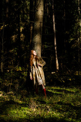 Young woman with long red hair in a linen dress gathering mushrooms in the forest in the bast basket